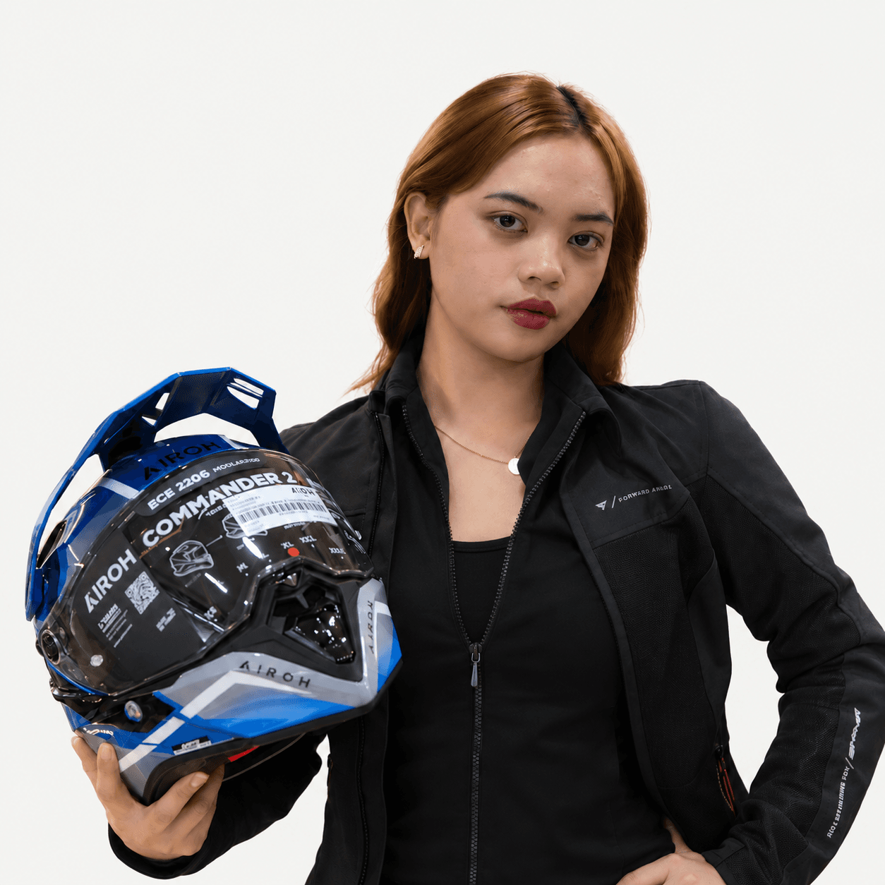 Rider in a black riding jacket holding a blue Airoh Commander 2 adventure helmet
